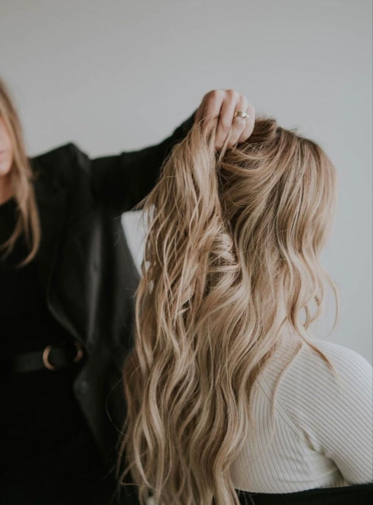 Person styling another person's hair with a focus on blonde hair extensions.